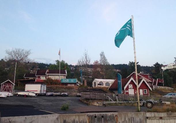 Figur 7. Bilde som viser eiendommen Husvikholmen 4 i dag sett fra vest med parkeringsareal for båt og bil i forgrunnen. Midt i bildet ser man Drøbakssund Seilforening med tilhørende annekser.