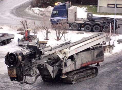 Comacchio MC 3000 på vei inn på tunet på Rud. Håndteringen utføres med klo og roto-tilt. Boring av φ711 rørpeler på flåte ved Gulli bru. Boring med RC-utrustning Holte URG borekrone for φ711 pelerør.