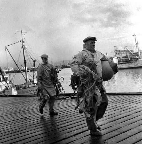 Sjómenn ganga á land með veiðarfæri sín í Vesturhöfninni. Í baksýn má greina Kolakranann og er myndin því tekin fyrir 1968 því þá var hann tekinn niður.