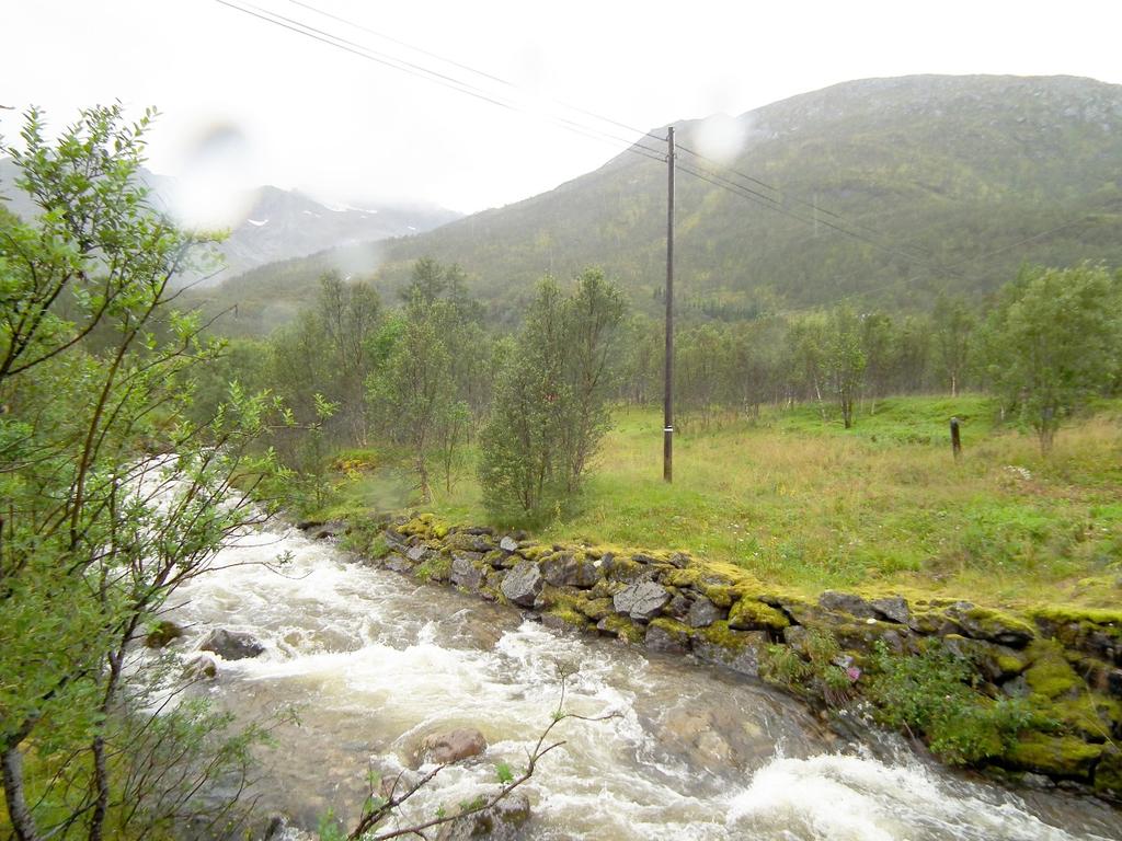 Rv.85 og vegen en fysisk og visuell barriere. Flere høyspentlinjer går på oversiden av vegen og bebyggelsen.