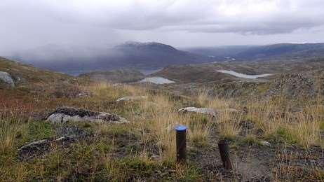 Jernrør etter gruveselskapet Nussir ASAs prøveboring stikker opp fra grunnen i Àsávaggi. I bakgrunnen skimtes Repparfjord.