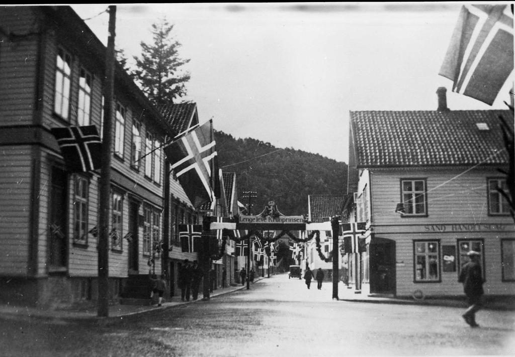 Frå Kronprinsbesøket på Sand i 1936. Portalen står mellom huset til Lene og butikken som Sand Handelslag overtok etter L. Hustoft. Ei vandrehistorie frå farfar sitt besøk hos Gunder og Marta i 1907.