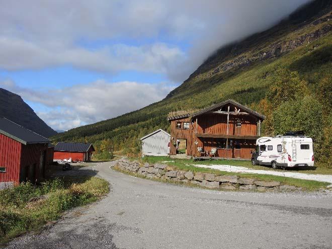 Vegen går mellom driftsbygninger/uthus og bolighusene og snuplass for enden av fylkesvegen oppleves som del av tunet.