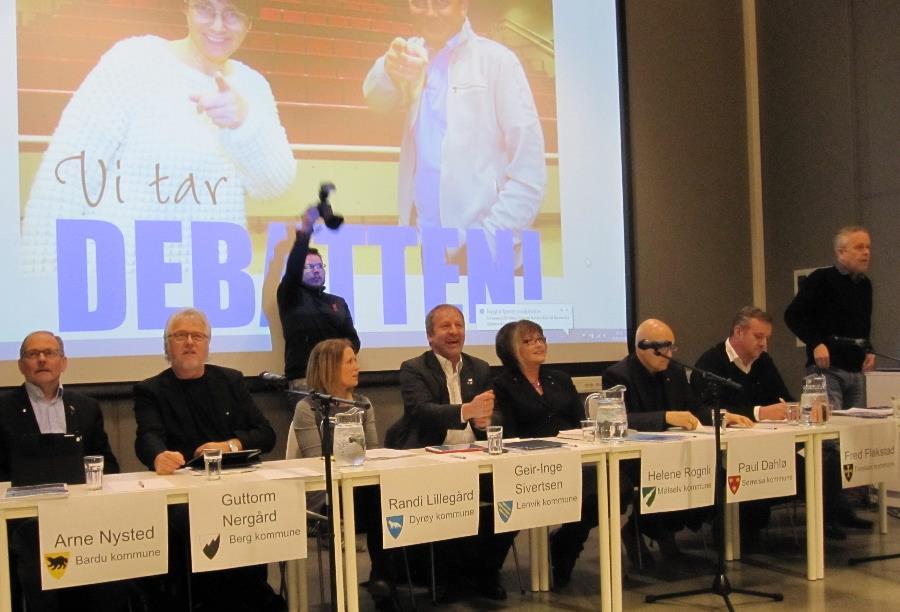 Et panel bestående av åtte ordførere har benket seg foran annonsen for debatten og en fotograferende journalist.