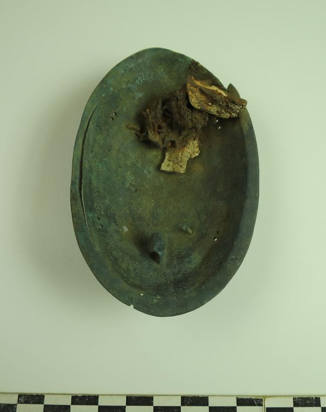 Figur 9: For- og bakside av innerskallet; C59153/2. På baksiden er det fastrustet brente bein og en liten jernring. Ringen kan ha hørt til smykkeopphenget eller spennens festeanordning.