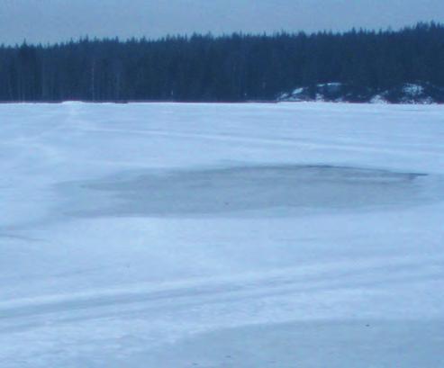 Islegging i flere etapper på en stille sjø. Det sentrale, dypeste området er ennå ikke islagt, nærmere land er et område med blank snøfri stålis, og langs land er det eldre snødekt is.