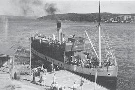 V i gjengir her et fotografi av D/S Nesoddtangen på vei inn til Aspond brygge. Den svarte røyken fra skorsteinen forteller at det var en kullfyrt dampbåt.