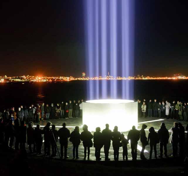 Friðarsúla Yoko Ono í Viðey með borgarljósin í Reykjavík í baksýn.