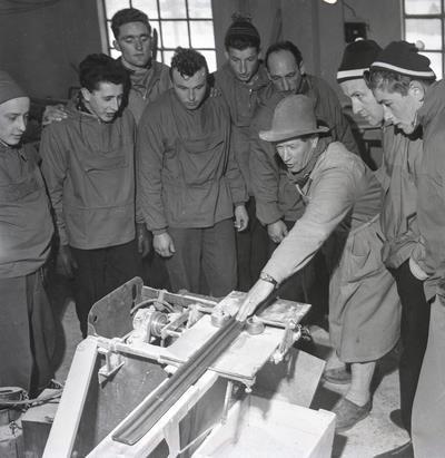 Italienske hoppere besøker skifabrikken, rundt 1950. Birger Ruud viser hvordan en styrerand under skien lages. Fotograf: Ukjent. Materialmangelen fortsatte.