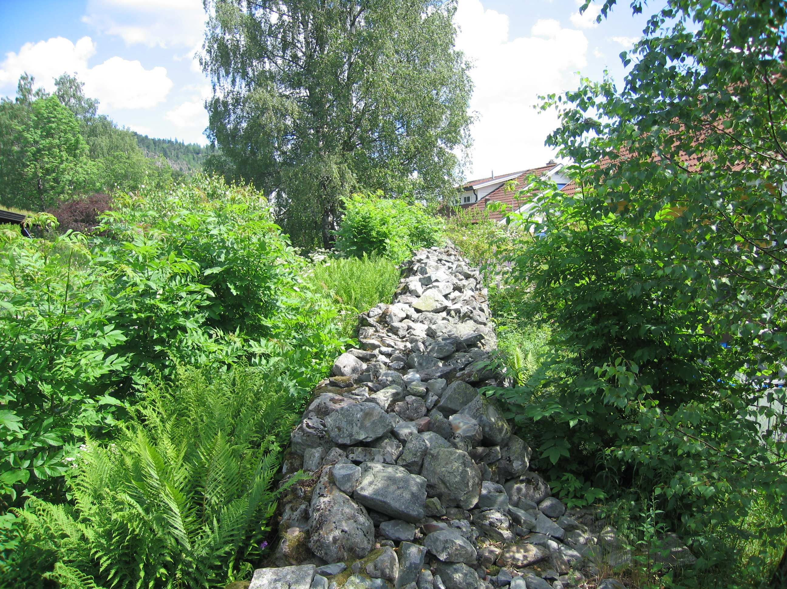 Foto 14: Steinmuren som ligger mellom eiendommene i øst, tatt mot nord. Fotoliste Foto 1: Bolighuset og hagen i Rykkinveien 24, tatt mot nord.