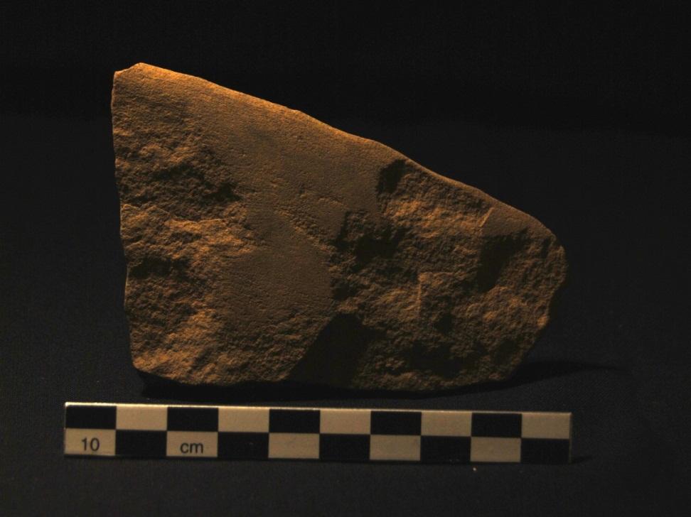 Figur 34: Fragment av sandsteinskniv, der slipespor langs eggpartiet er fremtredende og har opprinnelig omfattet til dels store deler av den ene overflaten. Fra flate 2, Vinterbrokrysset. Cf34433_160.